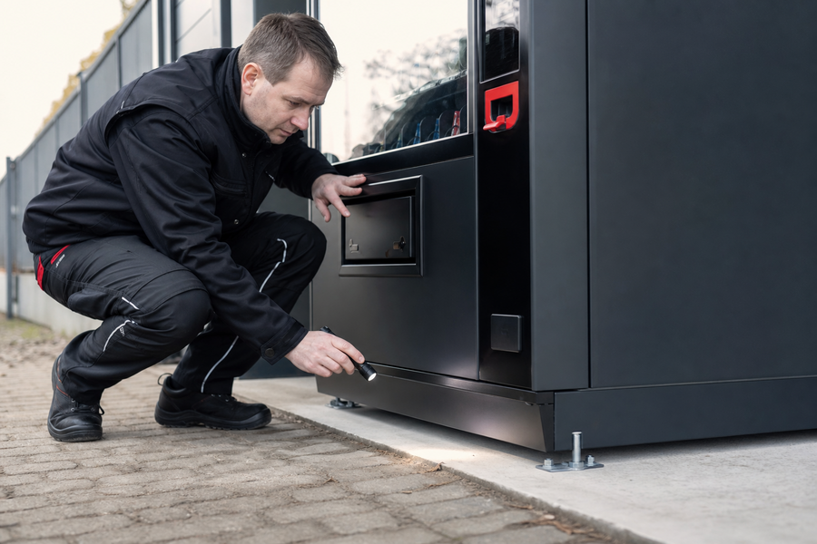 Fachkraft prüft Türsicherung und Bodenverankerung eines Verkaufsautomaten
