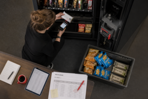 Betreiberin kontrolliert Chargen und sortiert Snacks nach FEFO in einen geöffneten Automaten